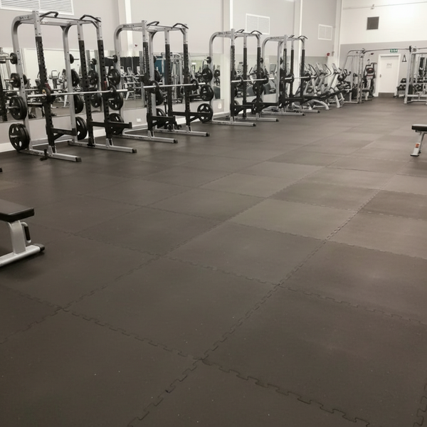 Commercial gym floor covered wall-to-wall with solid black rubber mats