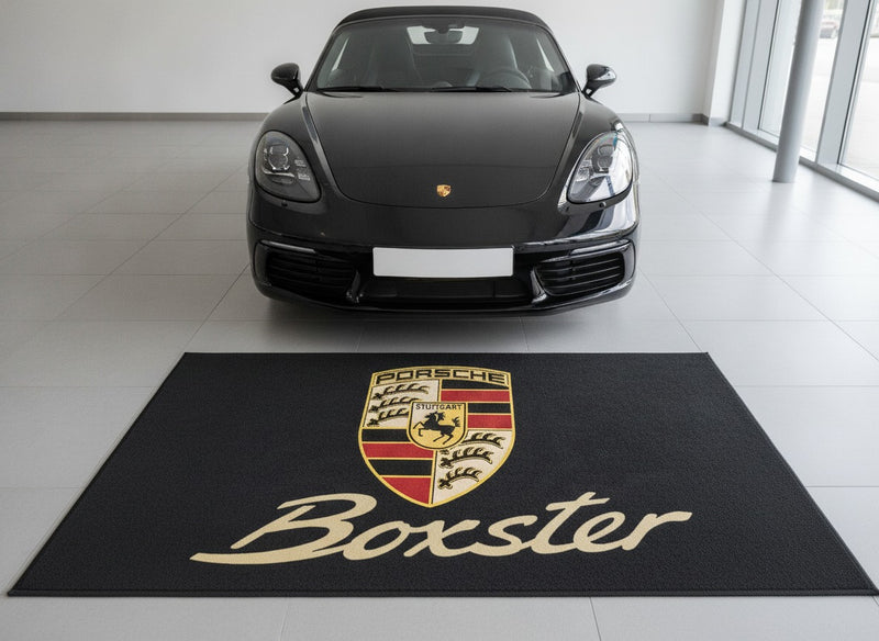 Porsche Boxster garage floor mat with crest and gold Boxster script in front of a black 718 Boxster in a bright showroom