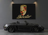 Porsche Boxster rug hung as wall art in a charcoal garage above a black 718 Boxster roadster